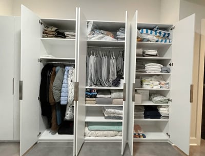 Neatly organized white wardrobe with folded linens, baby items, and hanging coats.