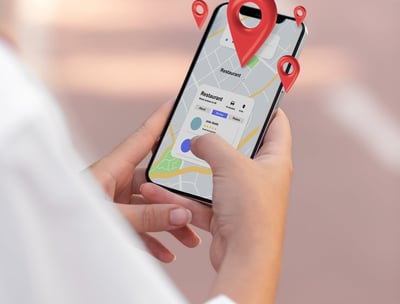 Mano sosteniendo un teléfono móvil con un mapa y varios pines de ubicación resaltando negocios local