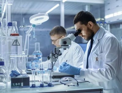 two men in lab coats and lab coats are looking at a microscope