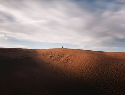two people standing on top of a large sand dune