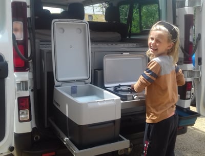 a young girl standing in front of a van with a coolerbox