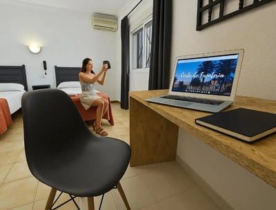 Habitación doble en Hotel San Vicente, con escritorio de madera, laptop y huésped tomando una foto.