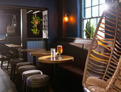 An egg chair next to some small round tables with drinks on 1 table