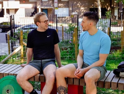 A personal trainer in a blue t-shirt sat outside talking to his client