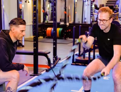 A man is exercising with battle ropes with a personal trainer