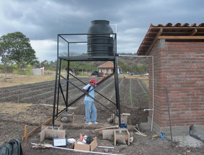 Jorge standing beneath a steel water tower used to feed the first two flush toilets in the community