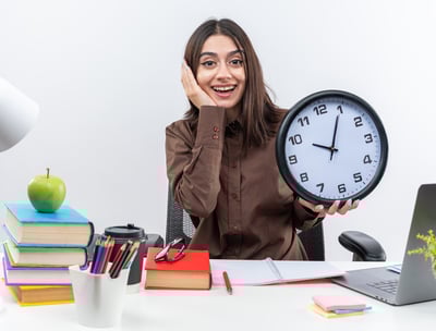 A young student holding a clock while studying depicting time management 
