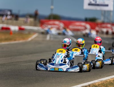 Plusieurs karts en course sur une piste, des pilotes portant des casques colorés et des karts marqués.