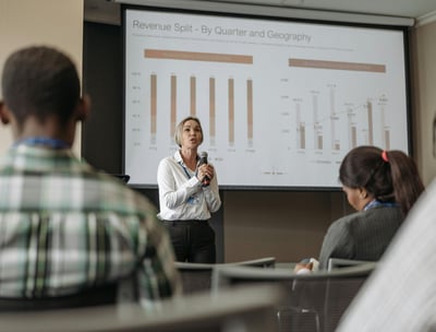 Mulher palestrando em evento, apresentando slides com equipamentos funcionando perfeitamente.