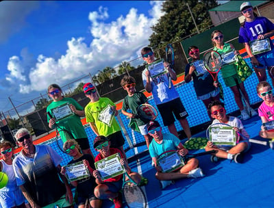 Kids holding rackets and summer camp certificates on tennis court.