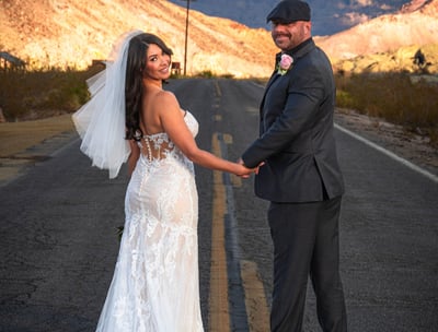 a bride and groom holding hands on a road