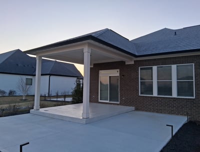 Covered patio with raised concrete floor under a roof with a larger uncovered concrete slab patio.