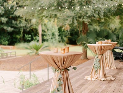 Mesa de coctel para eventos en el patio de una casa, decorada con manteles y veladoras