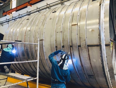 a man welding a large metal pipe in a factory