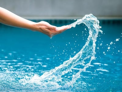 Close-up of a hand gracefully touching splashing water in a clear blue pool, symbolizing attentive and hands-on pool service.