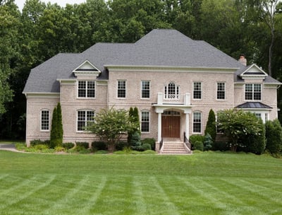 Large stately tan brick home on private lot with lush green grass in Virginia