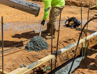 a man in a yellow jacket is pouring concrete into a concrete slab