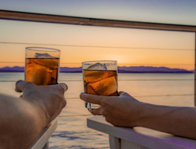 Couple sitting on deck at sunset with drinks in hand over the sea.