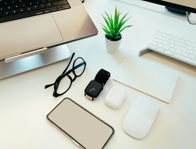 a computer monitor, keyboard, mouse, earpods, glasses, a plant showing the use of digital products