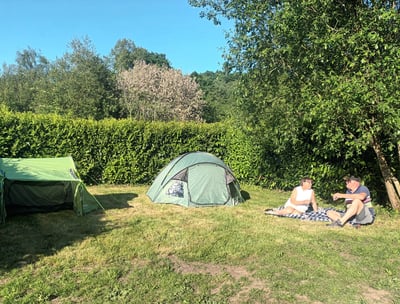 Two people relaxing on the grass beside a tent on a grassy pitch at Les Vieilles Forges campsite in 