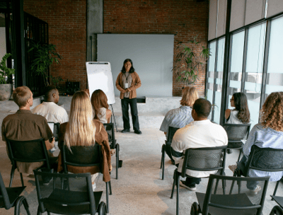 a woman in a brown jacket is standing in front of a group of people