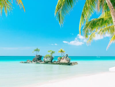 The famous rock formation in Boracay Island with white sand and tall palm trees, with clear blue sky