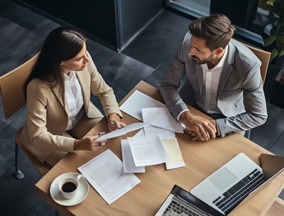 Two business people sitting at a table with papers and laptops