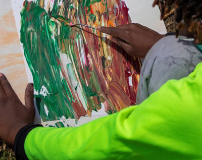 Young boy using a palette knife to smooth paint dabs over a paper.