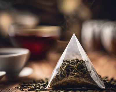On a wooden table pyramid shaped tea bag with cups of tea in it