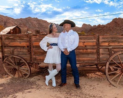 a man and woman in cowboy attire standing in front of a wagon