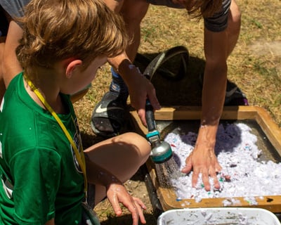 Teacher using a hose to spray shredded paper onto a screen with kids surrounding.