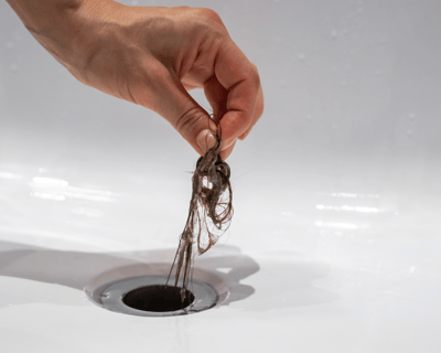 Main retirant des cheveux bouchant un drain de lavabo. Karukera Plomberie intervient pour le débouch