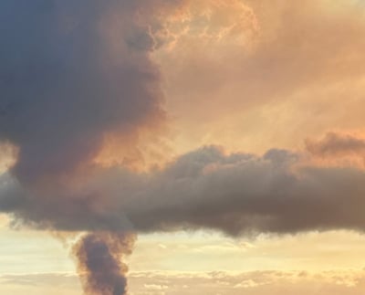 steam rising from vents caught in golden hour sunlight with kilauea eruption in the background