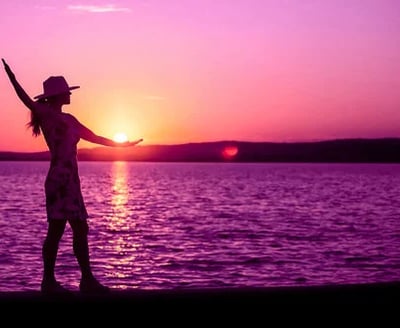 person practicing mindfulness for pain on a beach, using yoga or tai-chi. Purple sunset