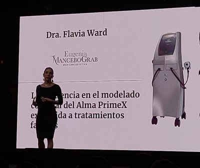 a woman standing on a stage with a large screen Dra Flavia Ward