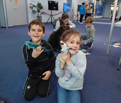 2 enfants avec des maquettes requins dans la main qui sourient
