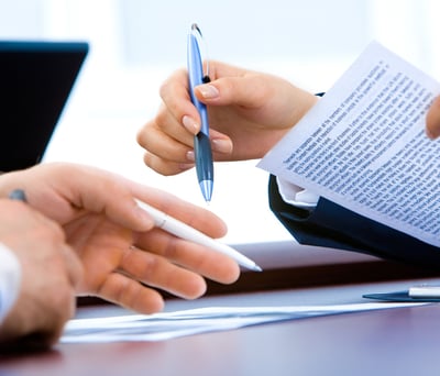 Hands hovering over a desk holding a pen and document