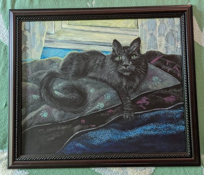 Cherry oak framed arcrylic portrait painting of a long haired black cat with very green eyes laying in his blanketed bean bag