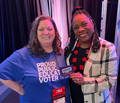 Woman in blue shirt standing with a black woman holding a campaign sticker