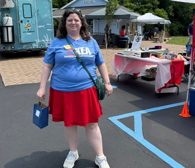 Woman in KEA tshirt standing in front of booths at the public library cultural pass kickoff