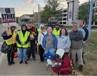 Large group of people standing with a on strike sign
