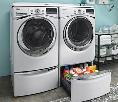 Front-loading washer and dryer in a laundry room with a storage drawer containing detergent and cleaning supplies underneath.