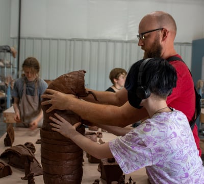 A teacher and middle school student holding a big clay creature up.
