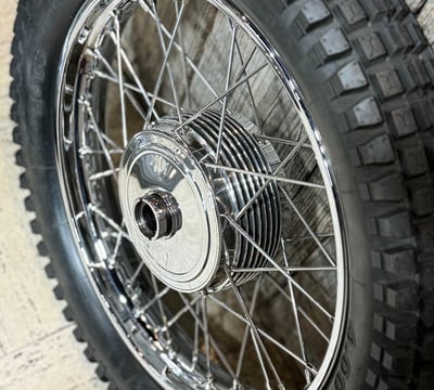 a motorcycle vintage hand polished wheel with a knobbie tire in front of wooden wall.