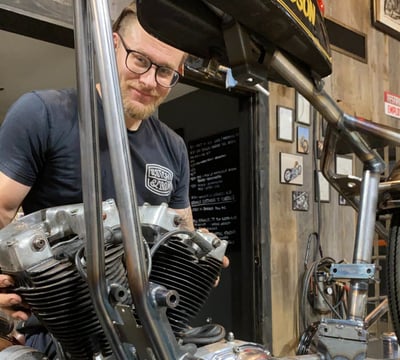 a man holding an engine behind a motorcycle frame.