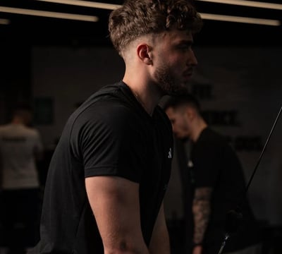 Barbat la sala, executa extensii pentru triceps la scripete, imbracat in negru.