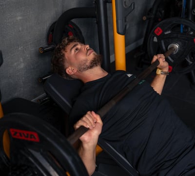 Barbat face impins la piept cu bara pe banca inclinata, echipat in negru.