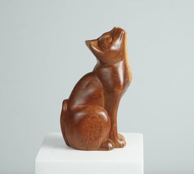 a wooden cat statue of a cat sitting sculpture on a pedestal