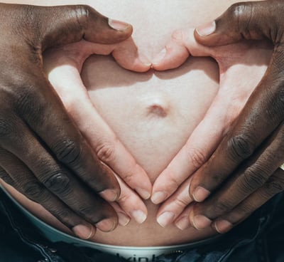 mains d'un ouple interracial  sur le ventre de la femme enceinte et  formant un cœur