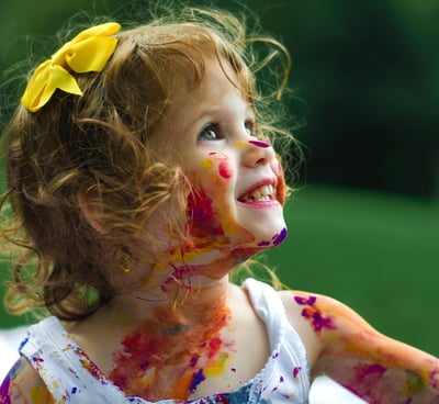Petite fille souriante, cheveux en désordres, noeud jaune, pleine de peinture- Pourquoi micro creche